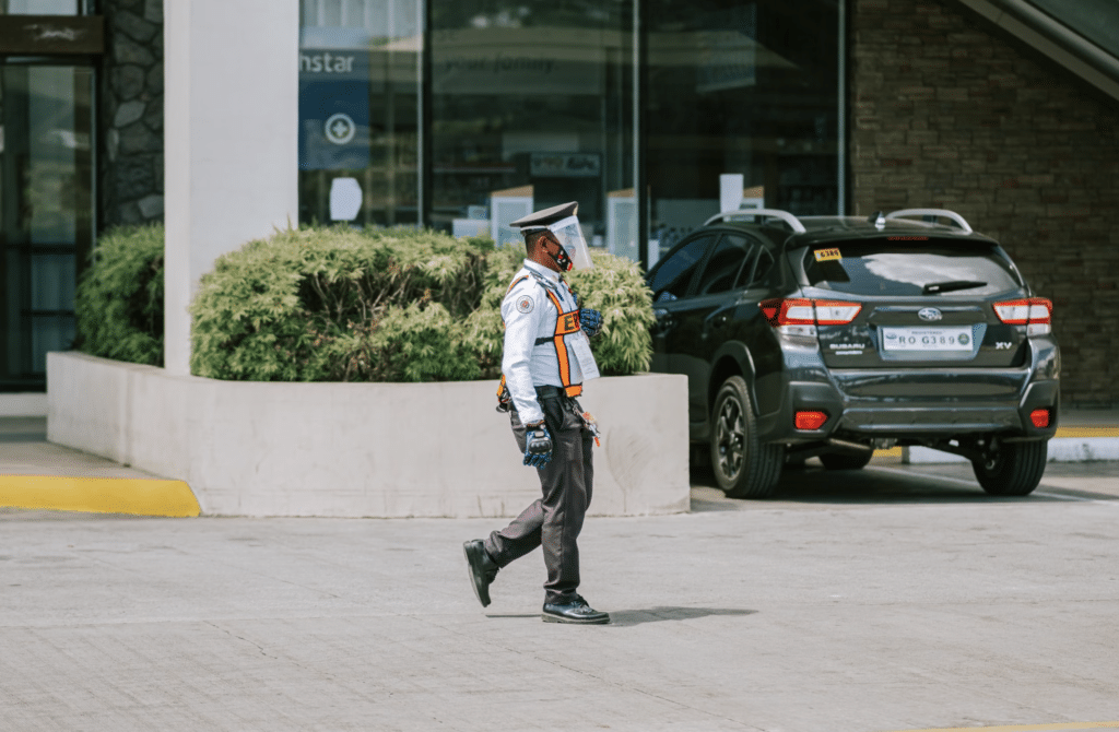 This photo shows a security guard walking near a business parking lot in daylight.