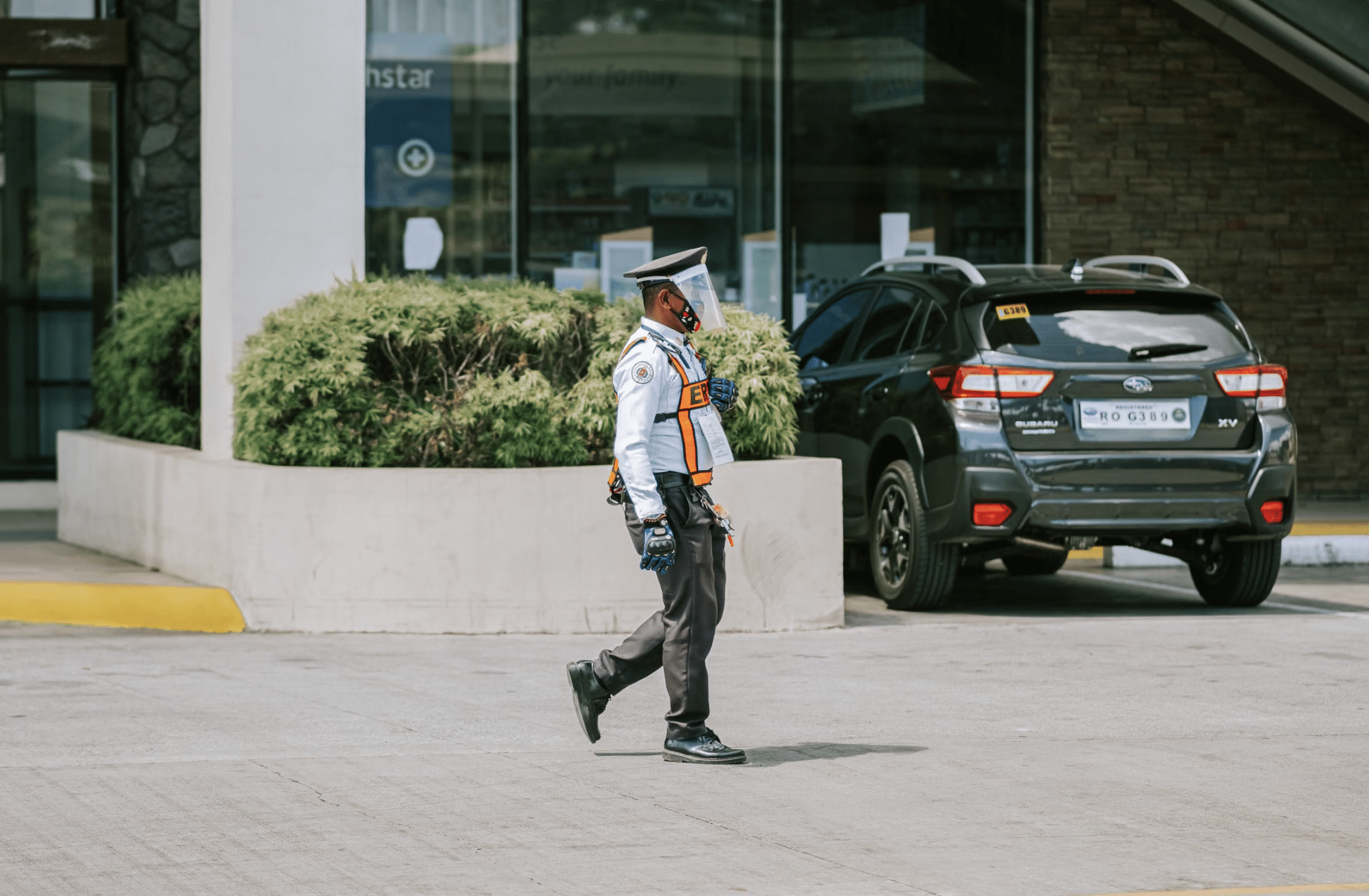 This photo shows a security guard walking near a business parking lot in daylight.